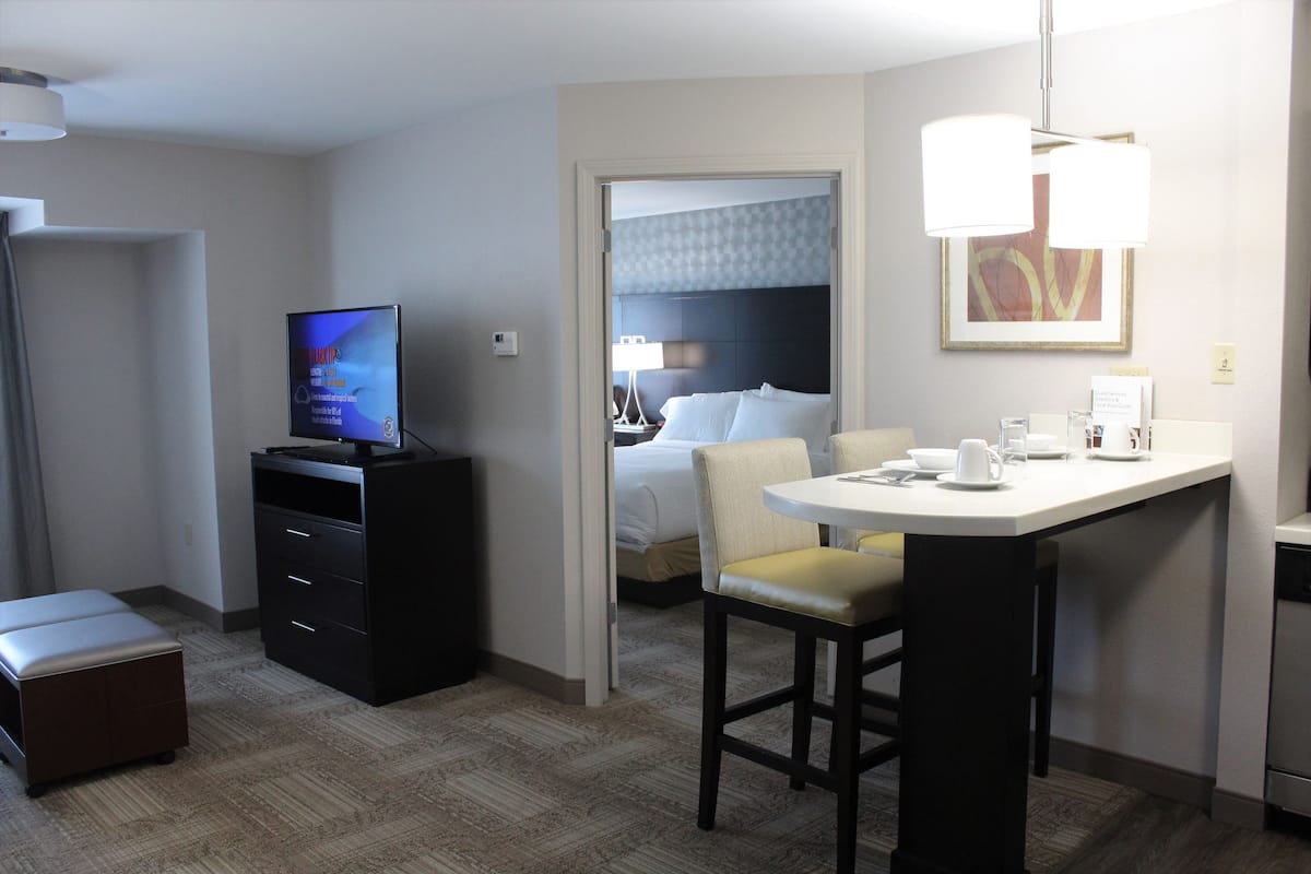 A hotel room with a bed, a desk with a computer, a chair, a small table, and a television.
