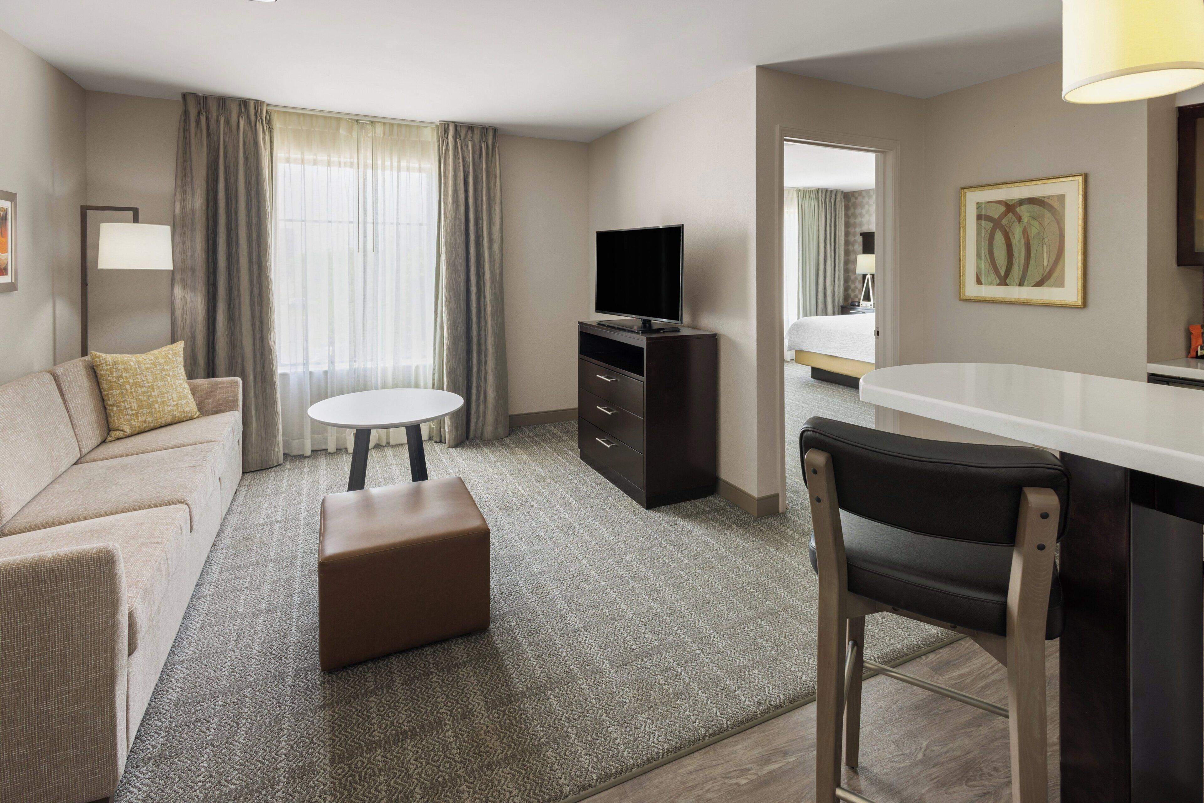 Une chambre d’hôtel avec un canapé, une petite table ronde, un téléviseur, un bureau avec une chaise et un lit en arrière-plan.
