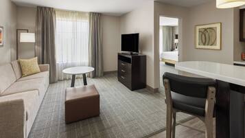 Une chambre d’hôtel avec un canapé, une petite table ronde, un téléviseur, un bureau avec une chaise et un lit en arrière-plan.
