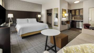 A hotel room with a bed, bedside tables, a small round table, a sofa, a kitchenette, and a TV.