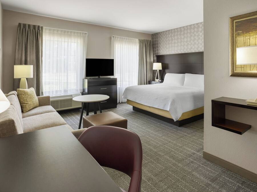 A hotel room with a bed, a desk, a chair, a television, and a lamp.