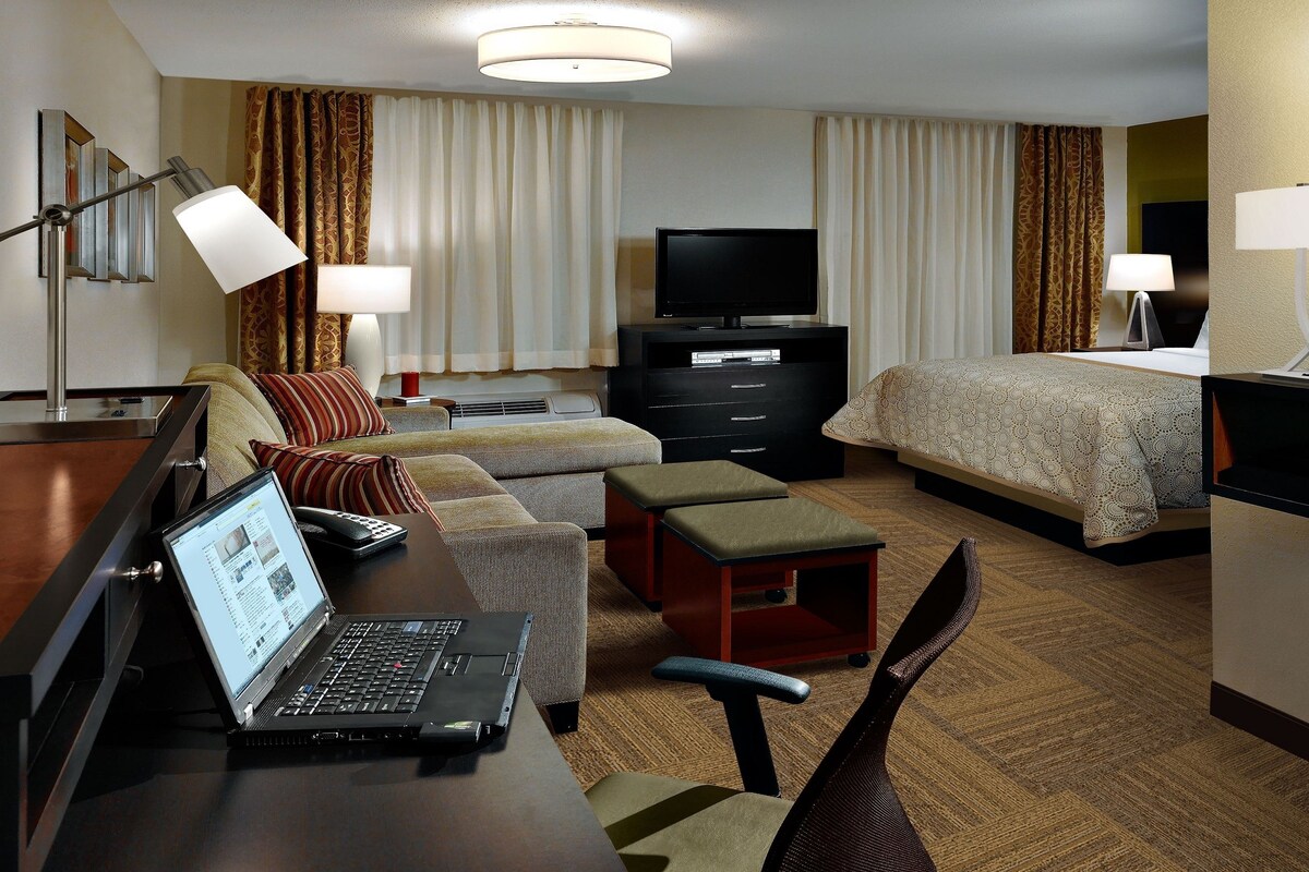 A hotel room with a bed, a desk with a laptop, a TV, and a sofa.