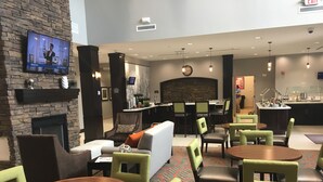 A hotel lobby with a fireplace, seating area, bar, and a television displaying an advertisement.