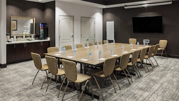 Una sala de conferencias con una mesa larga, sillas, dispensador de agua, máquina de café, televisor de pantalla plana y una pizarra.
