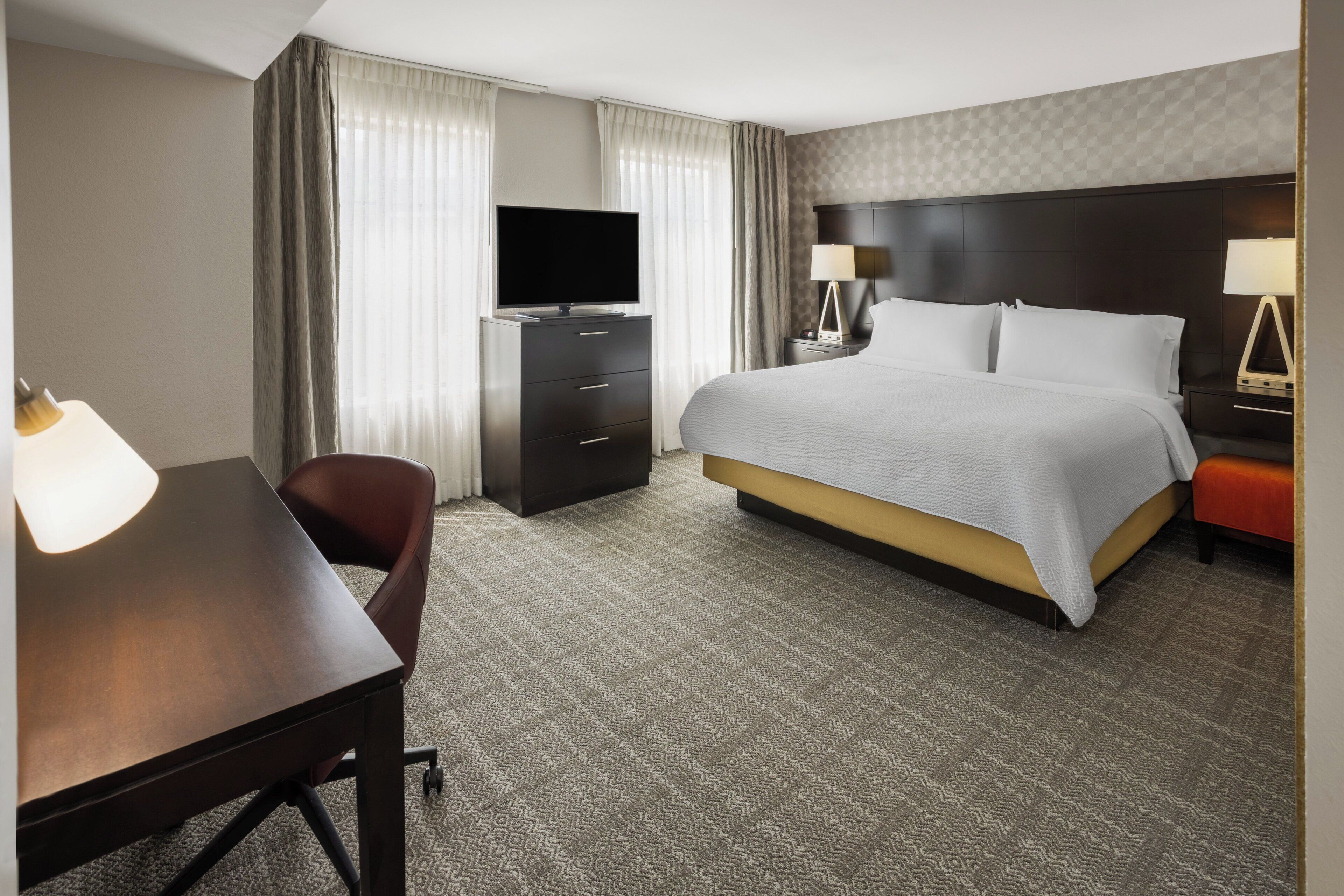 Una habitación de hotel con una cama, un escritorio, una silla, un televisor y una lámpara.
