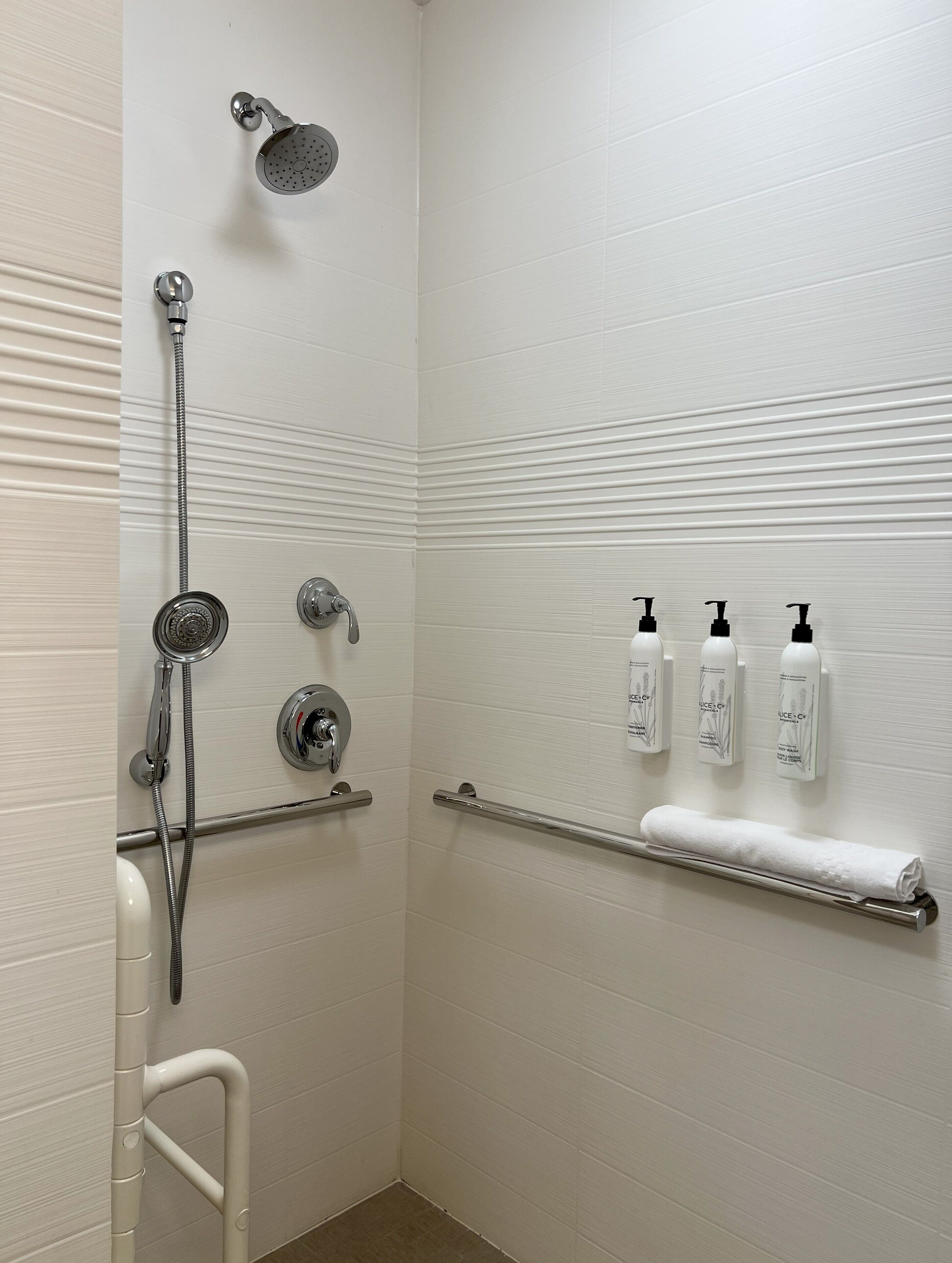 A bathroom with a shower, grab bars, and hand sanitizer dispensers.