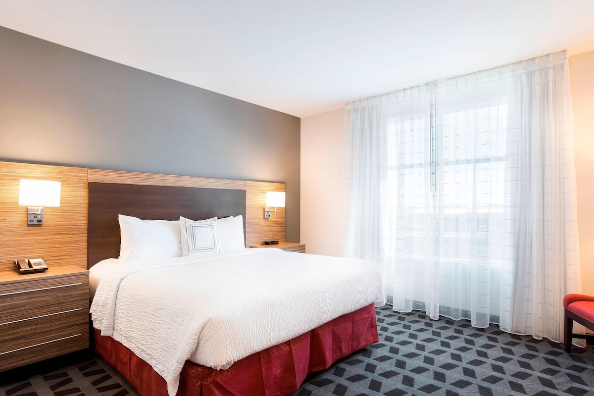 Een hotelkamer met een groot bed, twee bedlampen, een houten hoofdbord, een telefoon en een raam met dunne gordijnen.