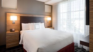 Habitación de hotel con una cama grande, dos mesitas de noche con lámparas, un cabecero de madera y una ventana con cortinas traslúcidas.