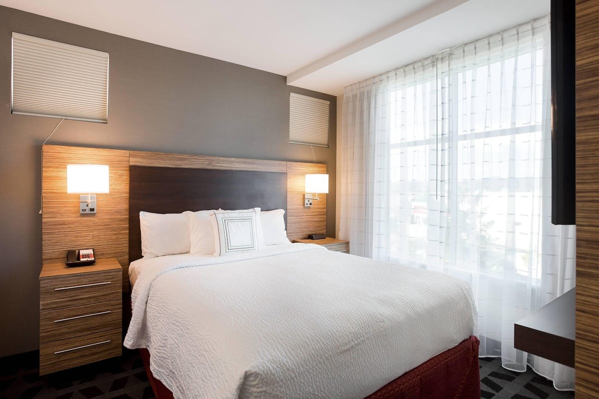 Hotelkamer met een groot bed, twee nachtkastjes met lampen, een houten hoofdeinde en een raam met dunne gordijnen.