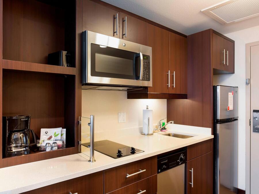 Una cucina moderna con mobili in legno, un forno a microonde in acciaio inossidabile, un frigorifero, una macchina da caffè e un lavello con rubinetto.