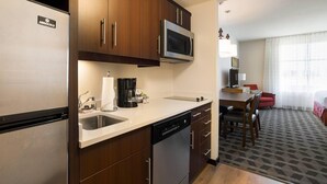 Cocina compacta con refrigerador, microondas y lavavajillas. Hay un comedor con mesa y sillas, y una cama en la habitación contigua.