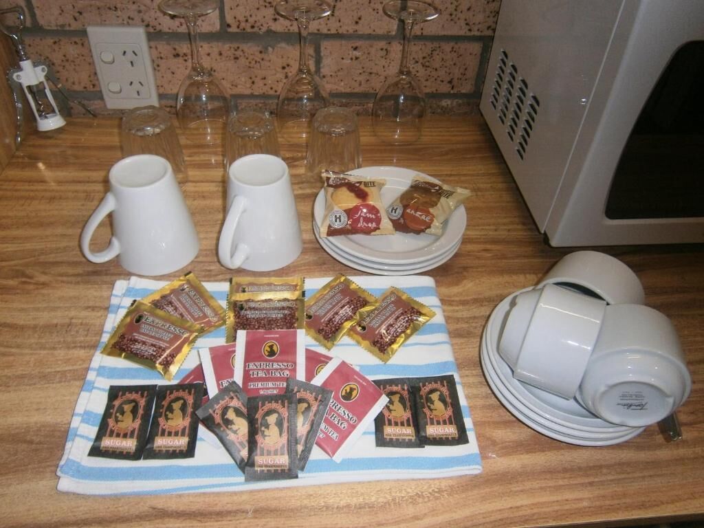 A kitchen counter with a coffee maker, two white mugs, a plate with food packets, and a towel with sugar packets.