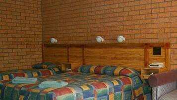 A room with two beds, a wooden headboard, and a small table with a lamp.