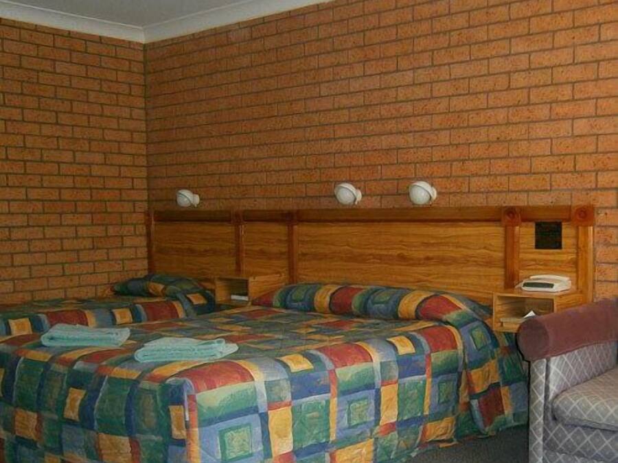 A room with two beds, a wooden headboard, and a small table with a lamp.