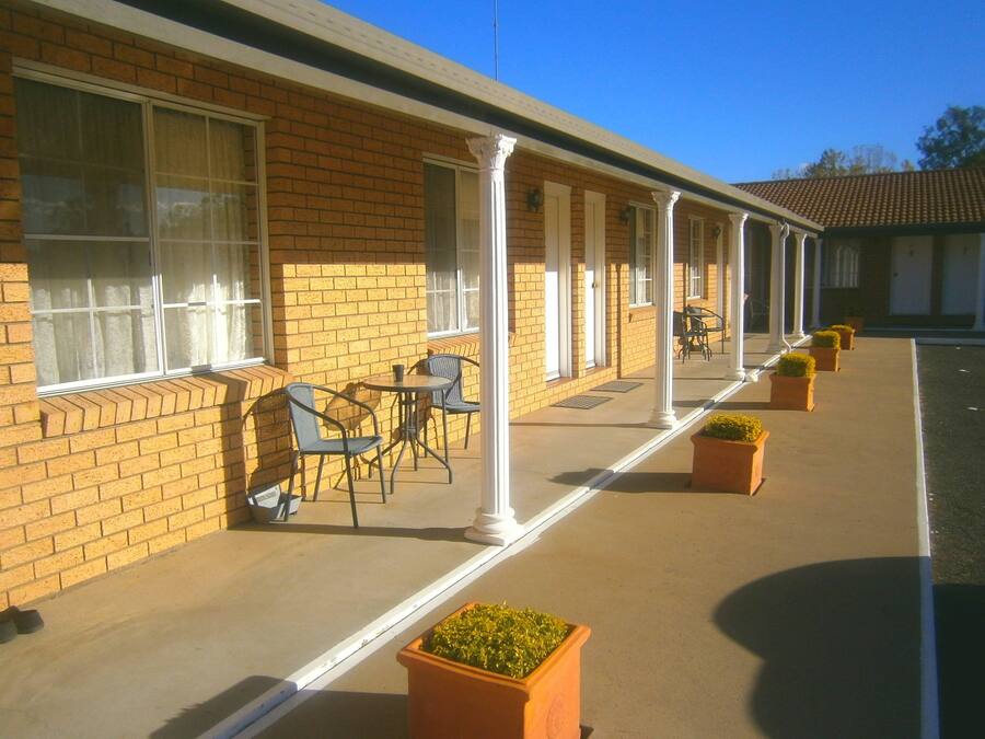 A motel with a brick facade, white columns, and outdoor seating with chairs and tables.