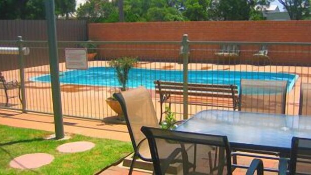 A fenced backyard with a swimming pool, a table, and chairs. - Aaron Inn Motel (Narrabri)