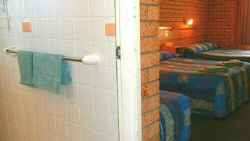 Habitació d'hotel amb zona de dutxa enrajolada, paret de maó i dos llits amb roba de llit colorida.