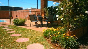 A patio area with a brick wall, a pool, and outdoor seating. - Aaron Inn Motel (Narrabri)
