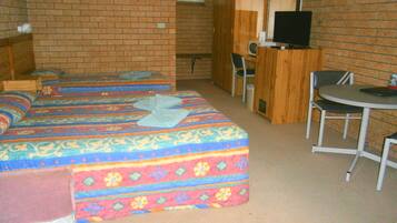 A room with two beds, a desk, a chair, a television, and a brick wall.