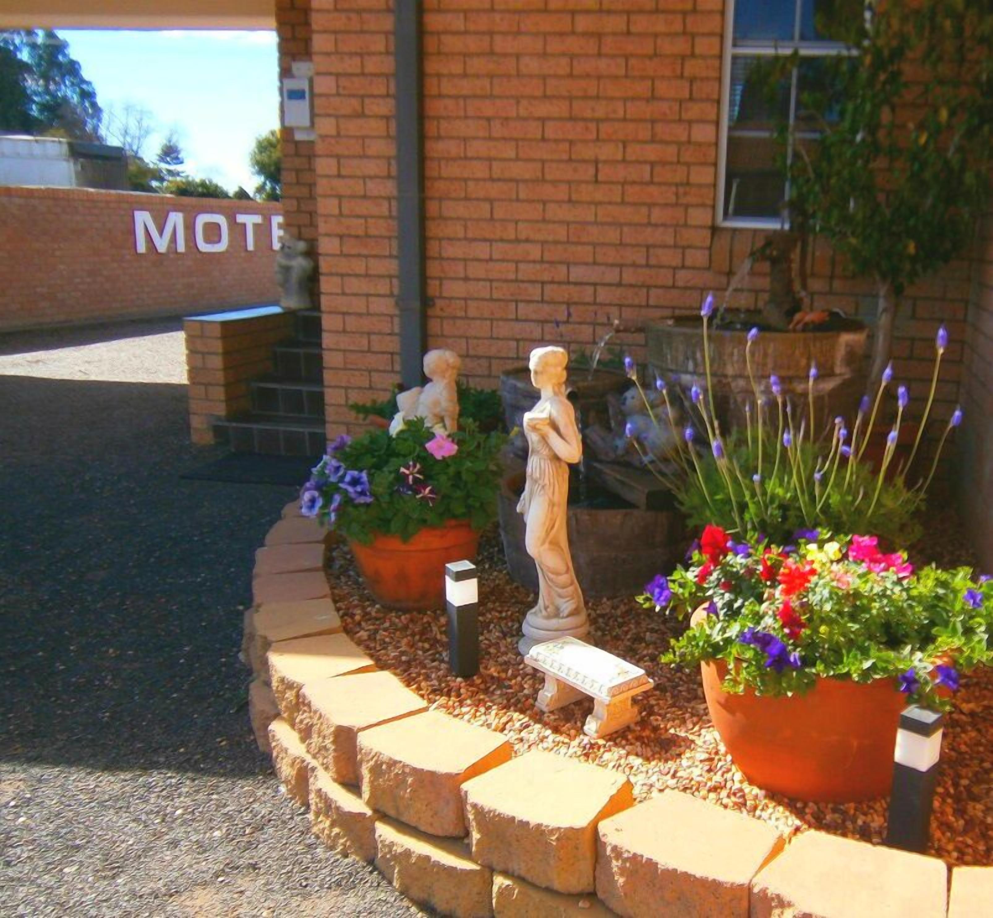 A brick building with a sign reading "MOTEL" and a landscaped area with potted plants and garden statues. - Aaron Inn Motel (Narrabri)