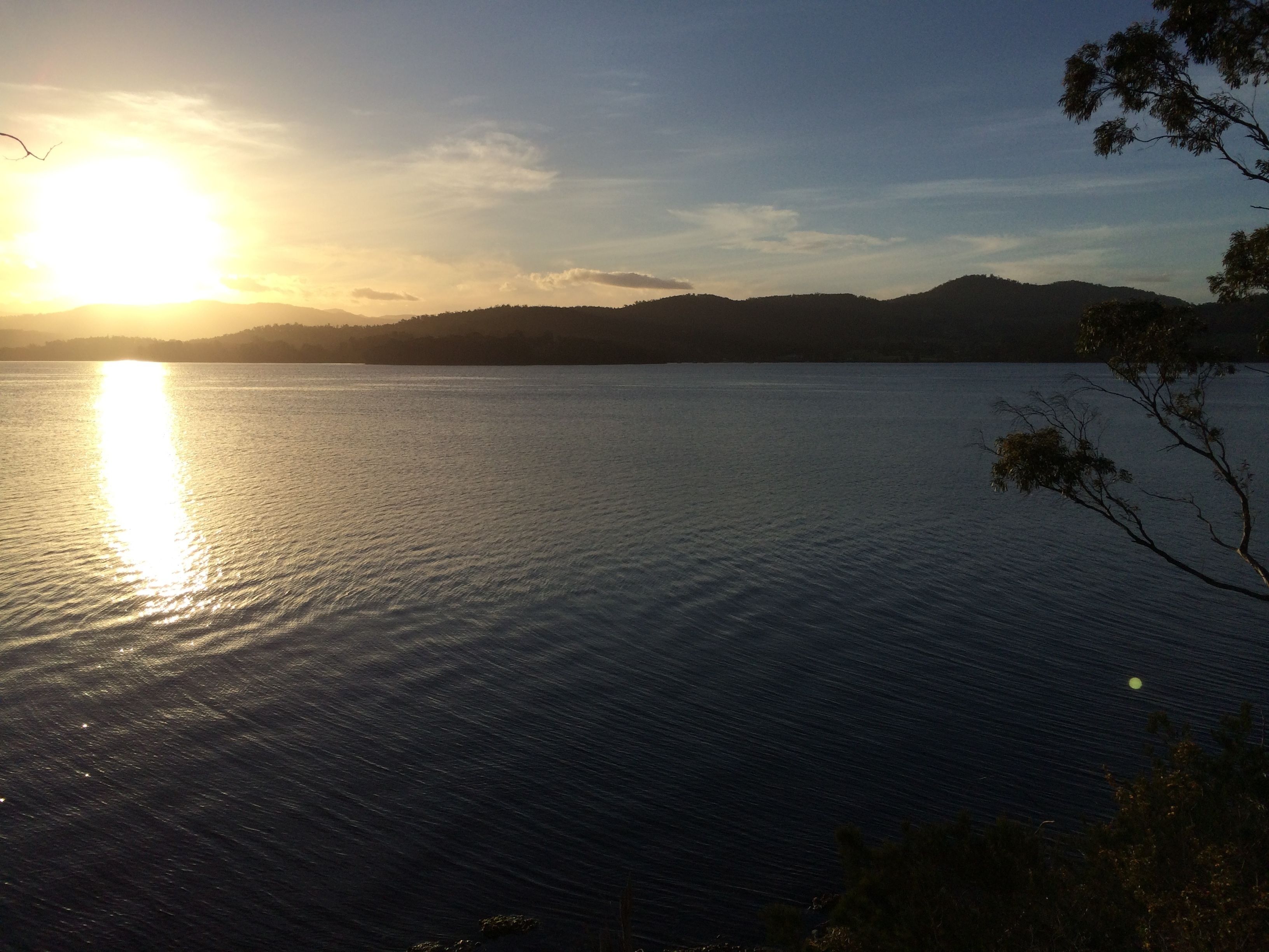 Un lago tranquilo al atardecer con cielo despejado y colinas lejanas.