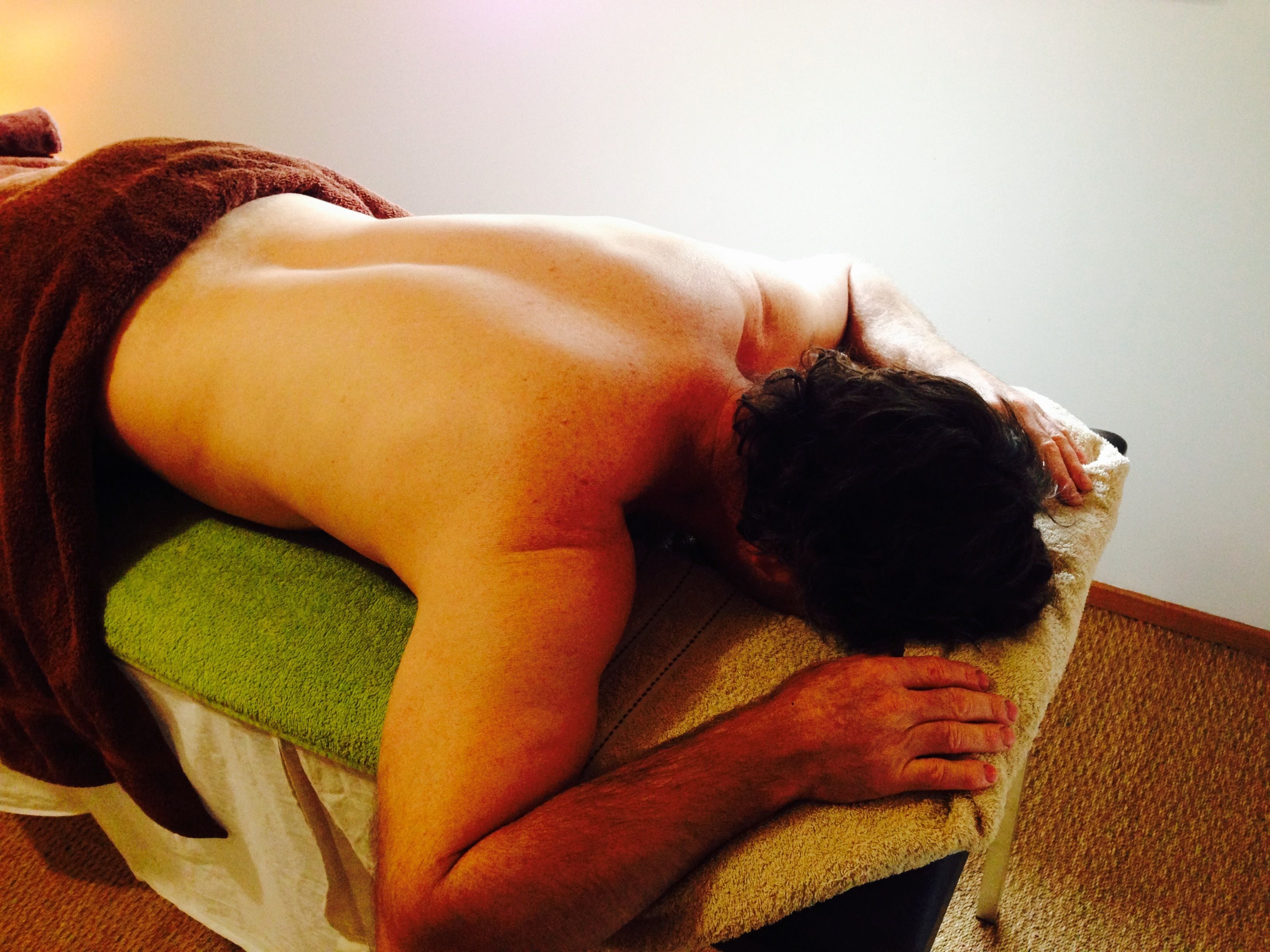 En person ligger på ett massagebord, och en handduk är draperad över personen.