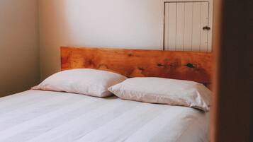 Een bed met een houten hoofdbord en twee kussens in een kamer met een witte deur op de achtergrond.