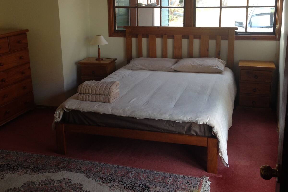 A bedroom with a wooden bed, a nightstand, a dresser, and a large window with a view of the outside.