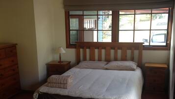 Un dormitorio con cama de madera, mesita de noche, cómoda y una ventana grande con vistas al exterior.