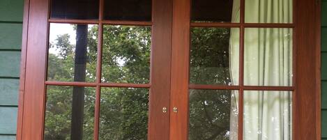 Una ventana de madera con múltiples divisiones, una pared exterior verde y vistas a árboles y un área con césped.