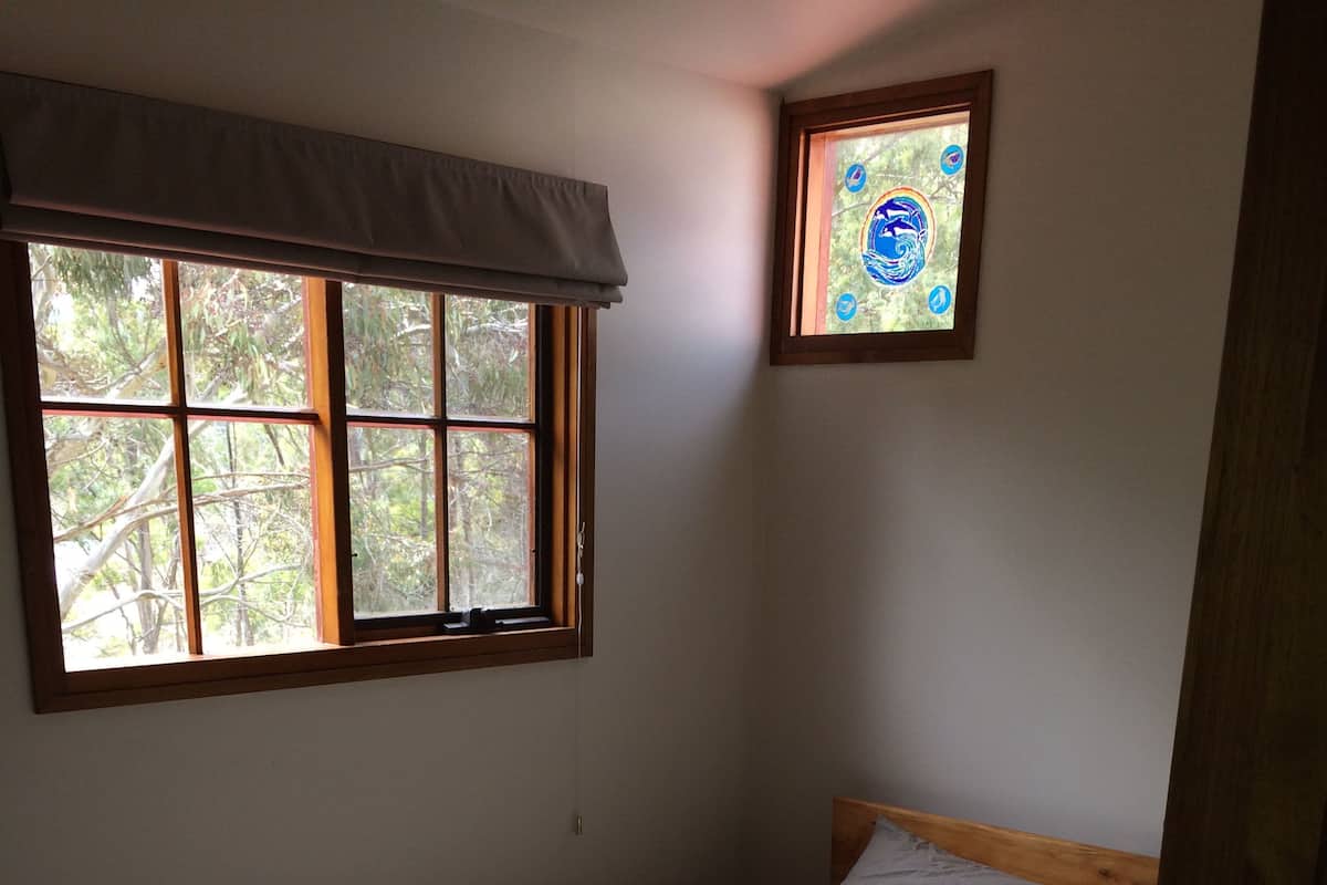 A single bed with a striped bedspread and a folded towel, a window with a view of trees, and a small framed picture on the wall.