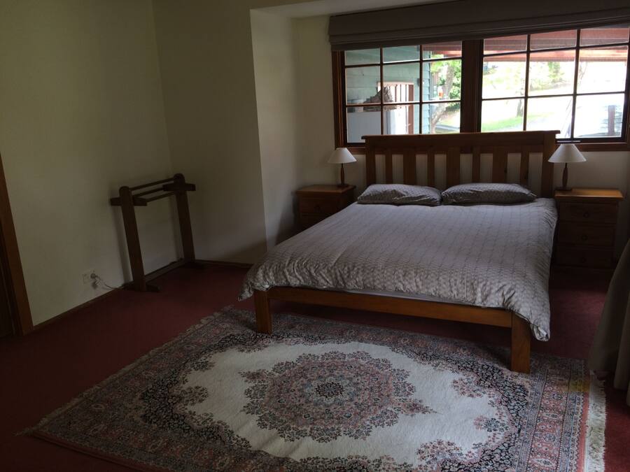 Een slaapkamer met een houten bed, twee nachtkastjes met lampen, een raam met uitzicht en een kamerbreed tapijt met dessin.