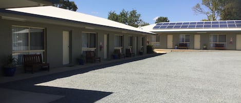 A motel with a gravel parking area, multiple rooms with windows, and a building with solar panels.