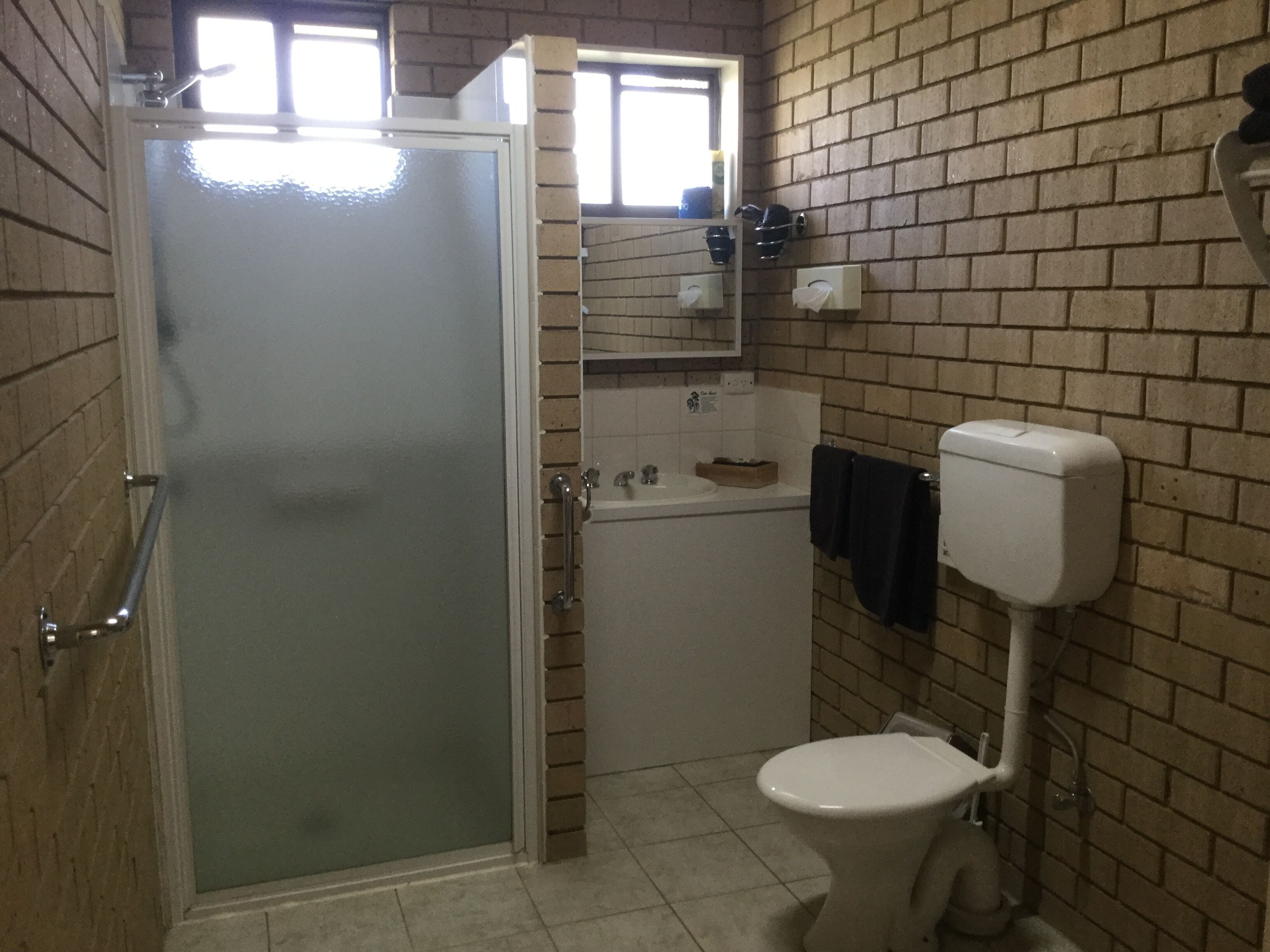 Un baño con puerta de vidrio, inodoro blanco, lavamanos y espejo encima.