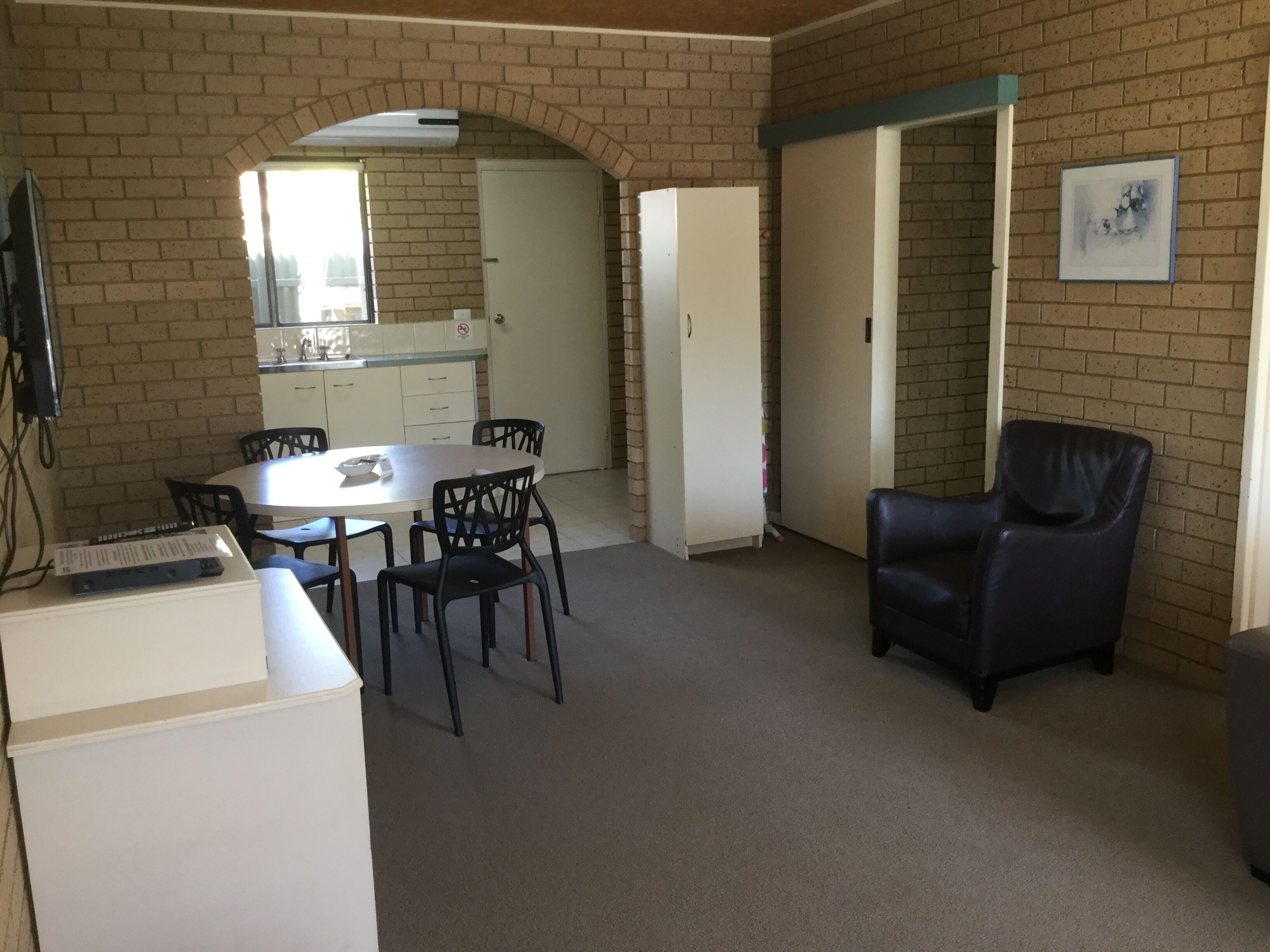 Ein Zimmer mit einem Esstisch, Stühlen, einem schwarzen Ledersessel, einem weißen Schrank und einer Ziegelwand.