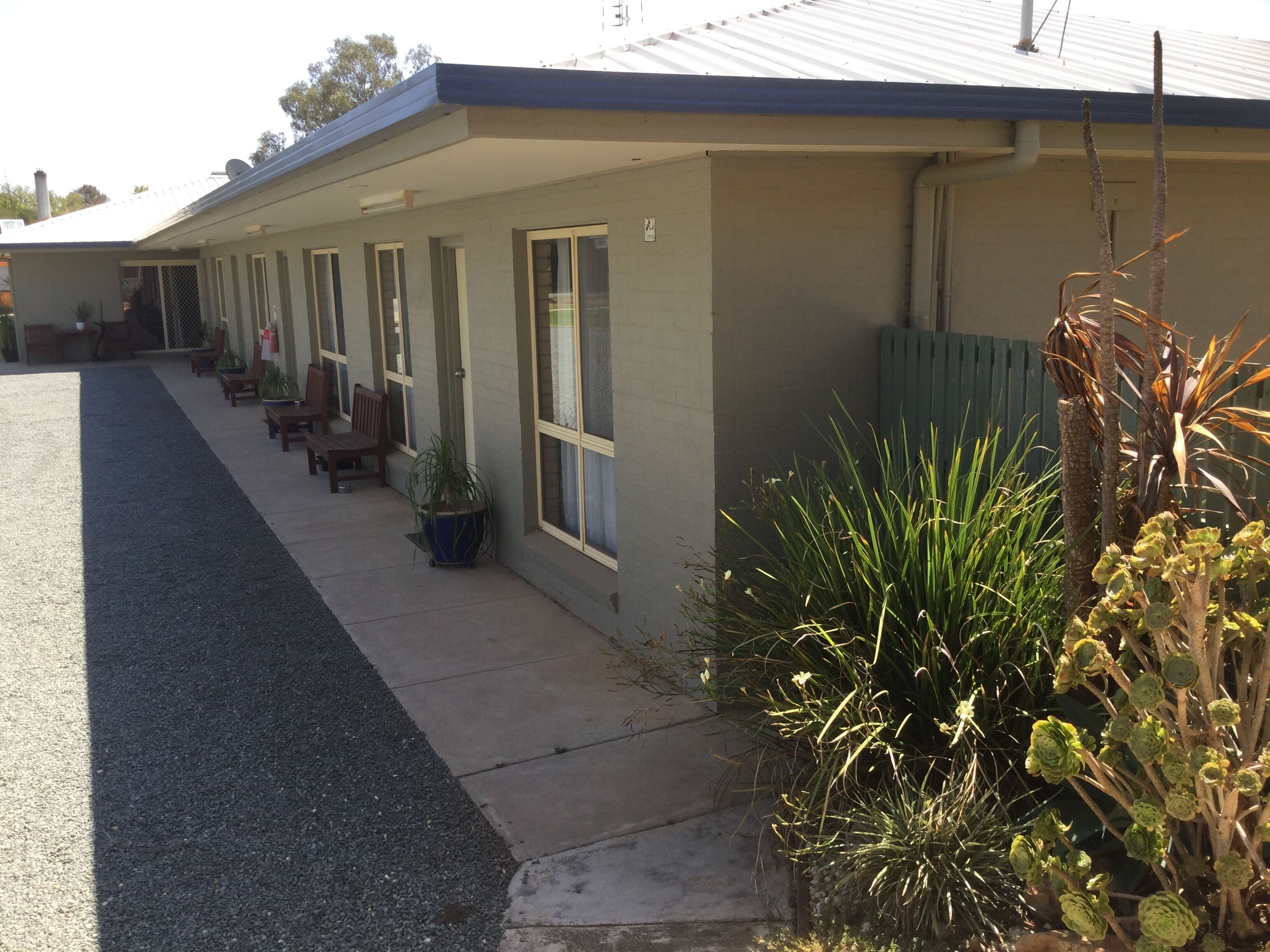 Fila de habitaciones de motel con puertas individuales, un área de estar cubierta al aire libre y plantas en macetas.