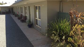 Fila de habitaciones de motel con puertas individuales, un área de estar cubierta al aire libre y plantas en macetas.