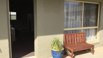 A wooden bench and a potted plant by a building entrance with a window.