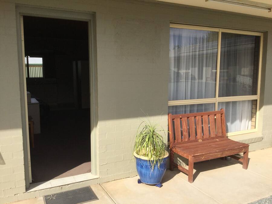 A wooden bench and a potted plant by a building entrance with a window.
