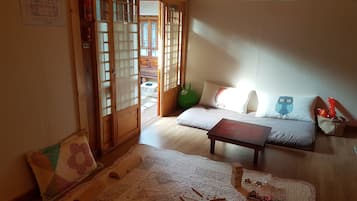 Um quarto japonês tradicional, com tatames, uma mesa de madeira baixa, um sofá com almofadas e uma porta deslizante que dá para uma área externa.