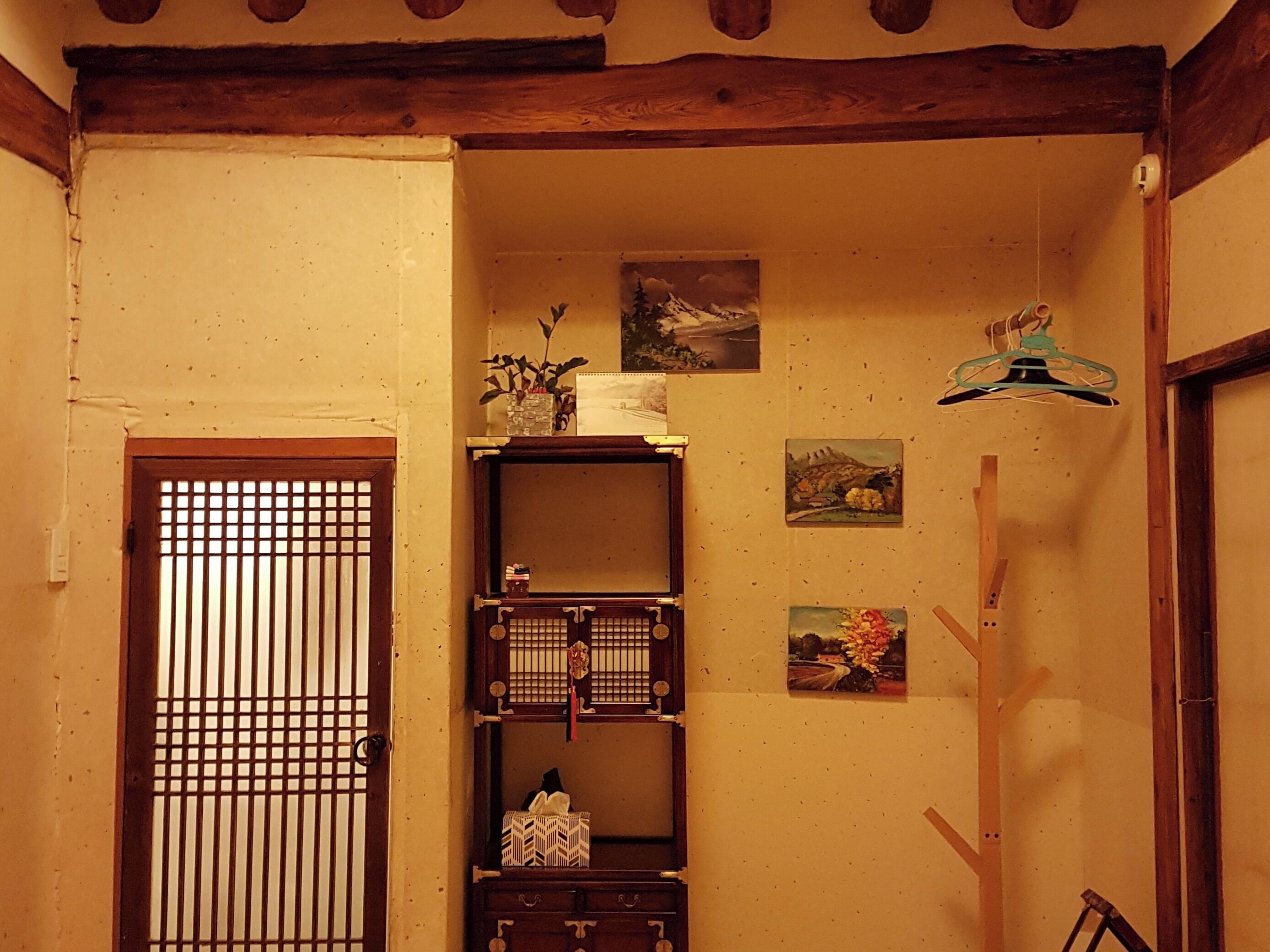 A traditional Japanese room with tatami flooring, a shoji screen door, a wooden shelf with decorative items, and a hanging light fixture.