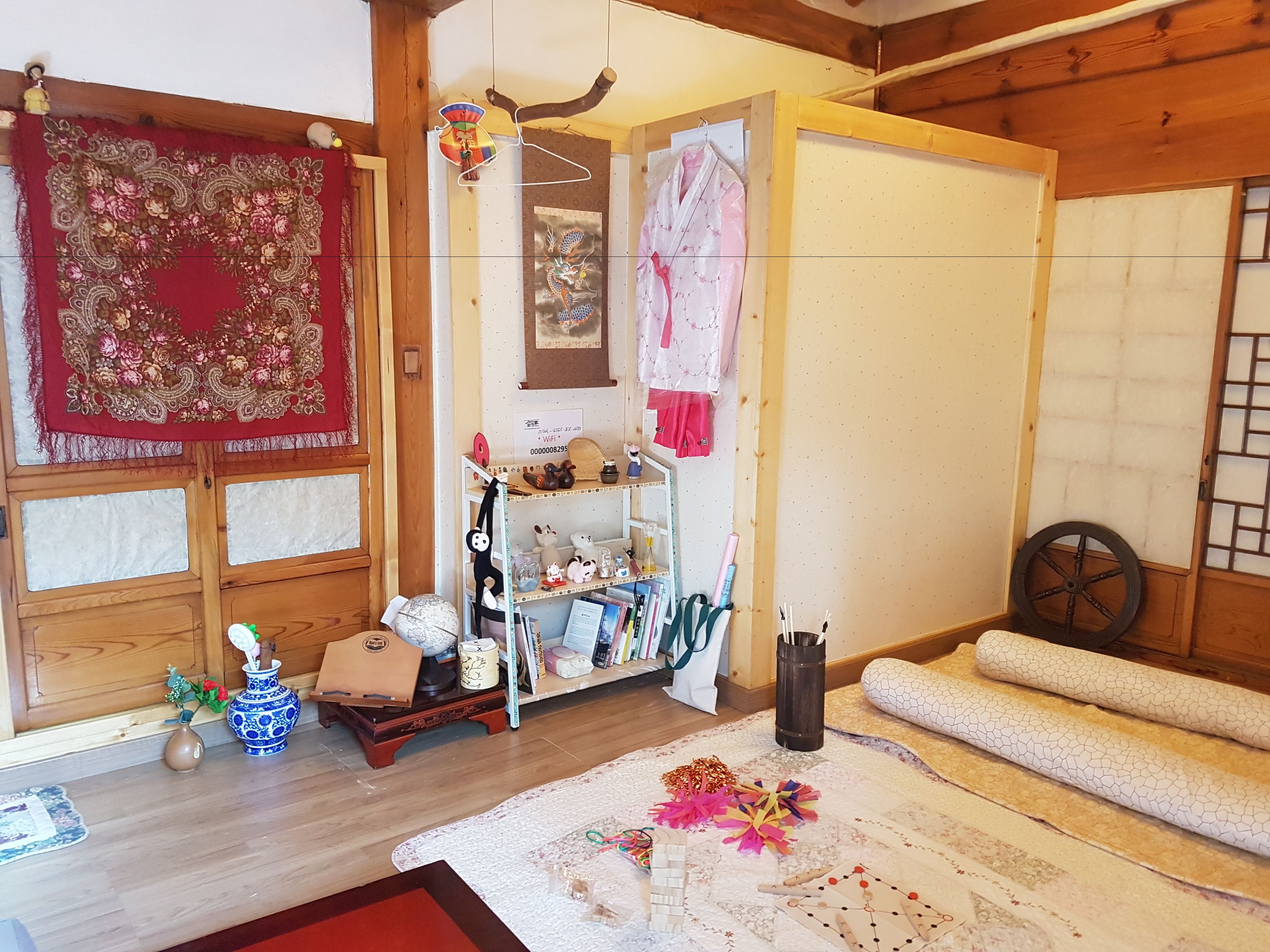Ein traditioneller japanischer Raum mit Tatami-Boden, Shoji-Schirm, einem Holzbodenregal mit diversen Gegenständen und einem Kleiderständer mit Kleidung.