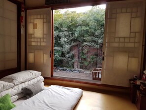 A room with a bed, pillows, and a sliding door leading to an outdoor area with bamboo plants and a brick wall. - Gongsimga Hanok Guesthouse (Seoul)