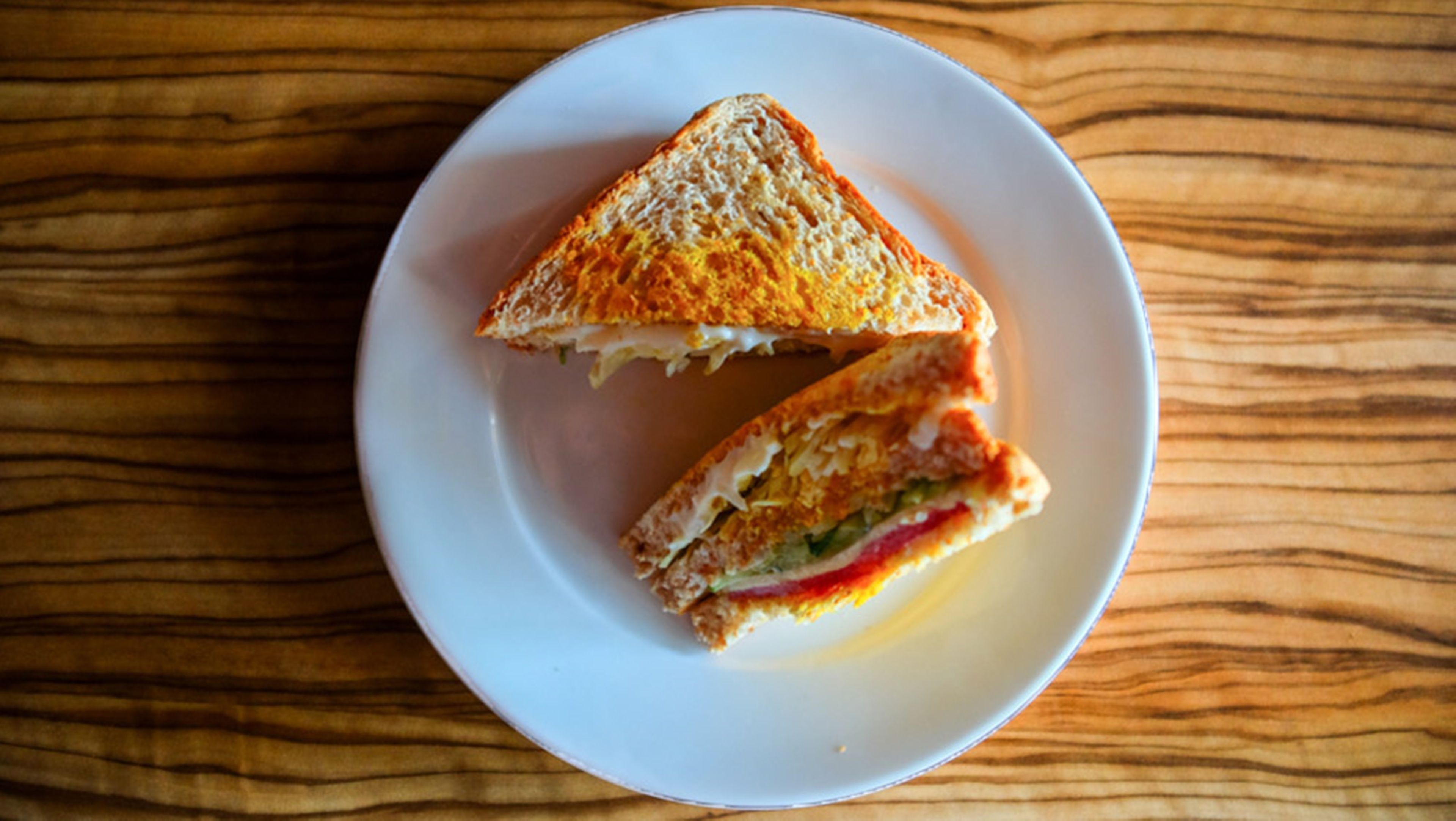 A sandwich on a white plate on a wooden table.