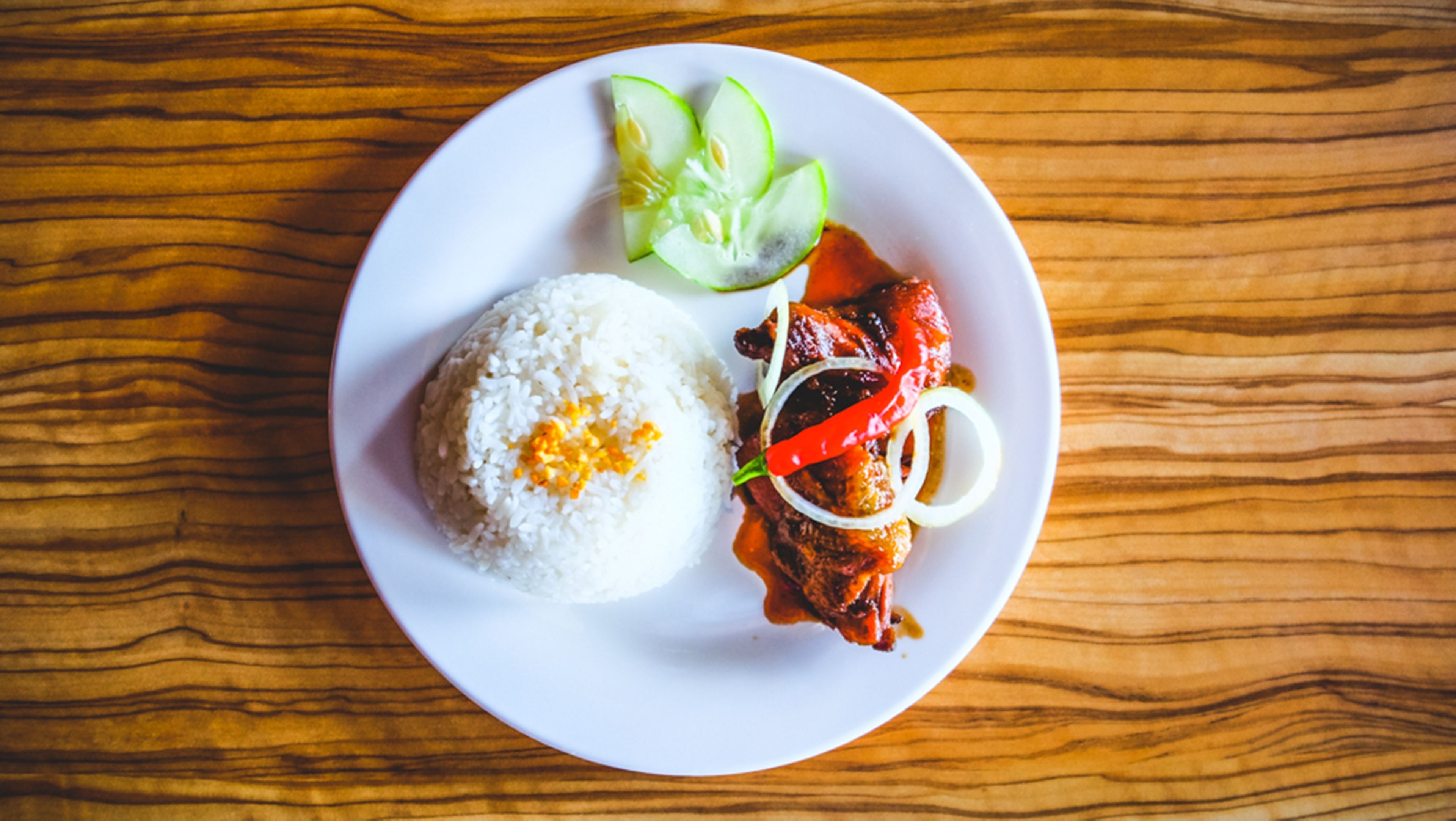 Un plato de comida con arroz, carne a la parrilla y verduras sobre una mesa de madera.