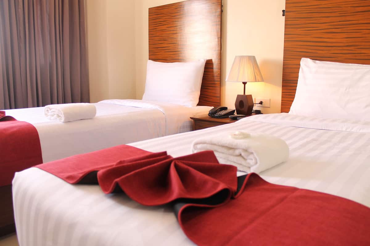 A hotel room with two beds, each with white linens and red accents, a wooden headboard, a bedside table with a lamp, and a telephone.