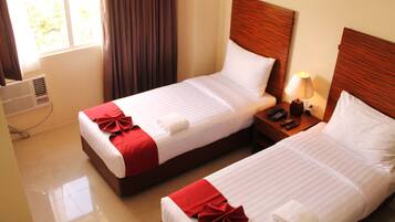 Two neatly made beds with red and white linens, a bedside table with a lamp, and a window with curtains.