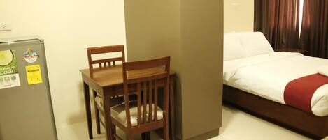 A hotel room with a bed, a wooden table with a chair, and a refrigerator.