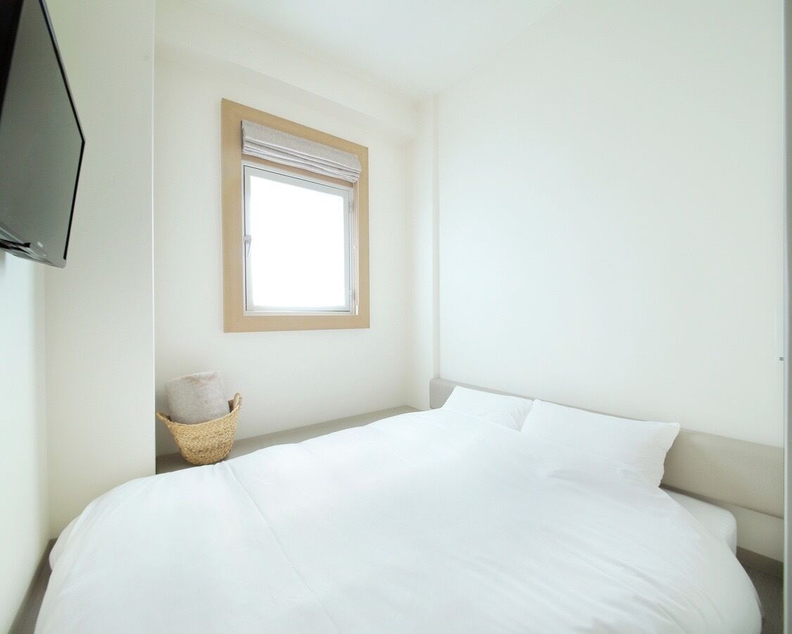 A bedroom with a bed, a window, a television, and a basket.