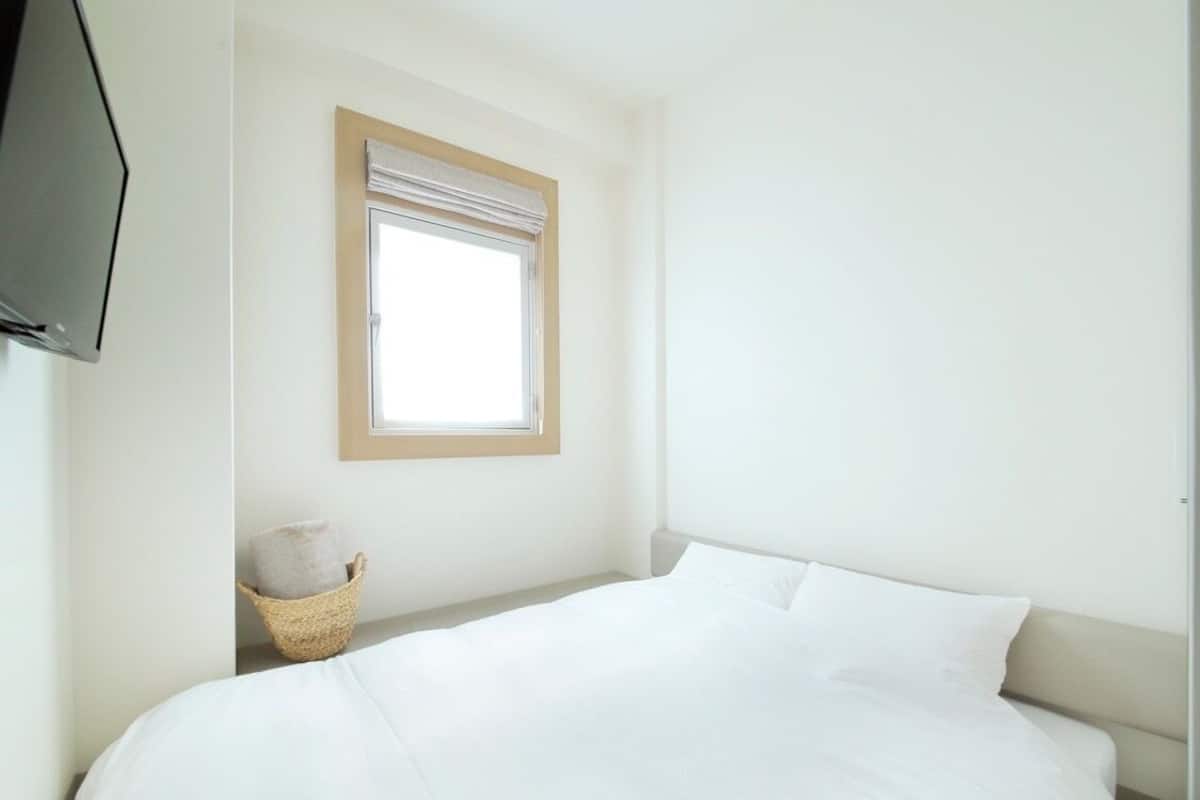 Une chambre à coucher avec un lit, une fenêtre, une télévision et un panier.